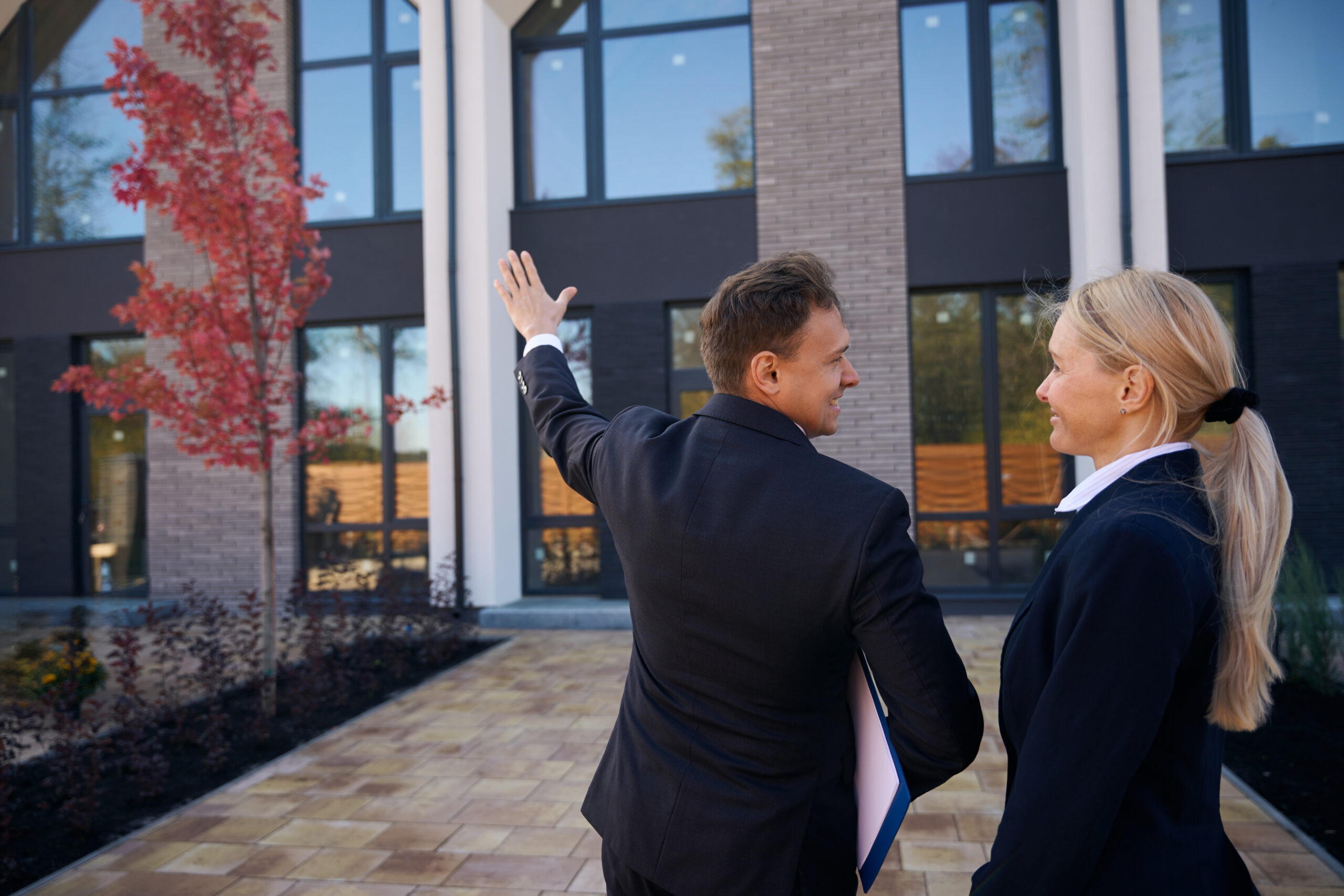 Realtor standing near building and showing it to client Brokerage services